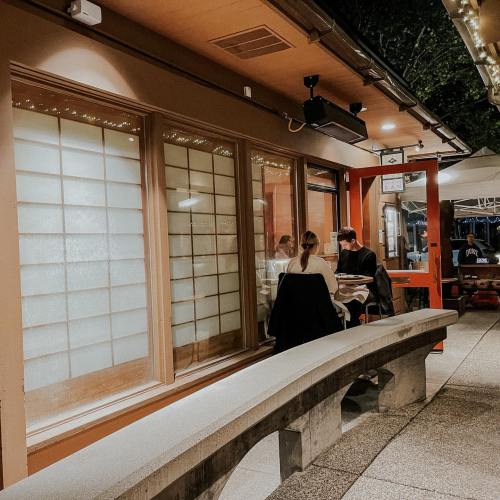 A couple sits at a table inside a cozy restaurant with large windows, illuminated by soft lights at night.