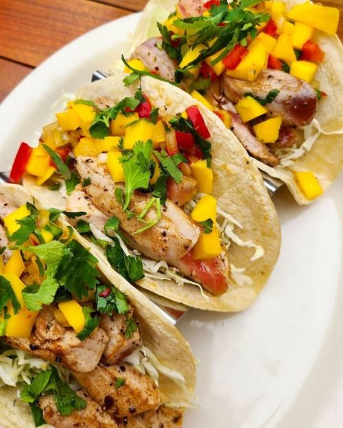 Three grilled chicken tacos topped with mango, red pepper, and cilantro on a plate.