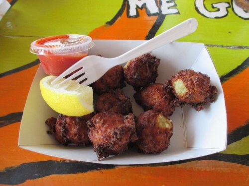 A serving of golden-brown fritters with a lemon wedge and a small cup of red sauce on a colorful table.