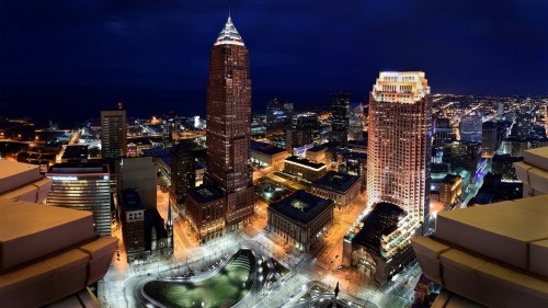 Aerial view of a city skyline at night, featuring illuminated buildings and streets against a dark sky.