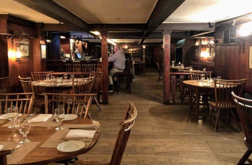 Cozy restaurant interior with wooden tables, chairs, and a bar in the background, softly lit for a warm atmosphere.