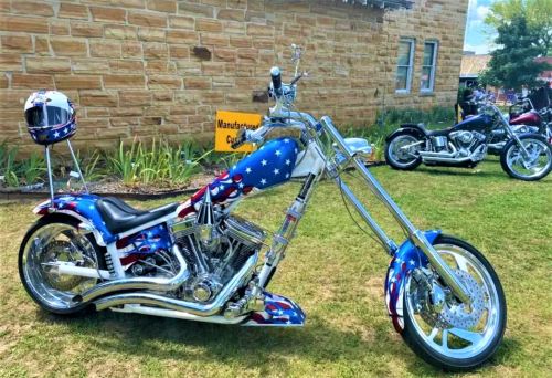 A custom motorcycle with a blue and red design featuring stars, parked on grass beside another bike.