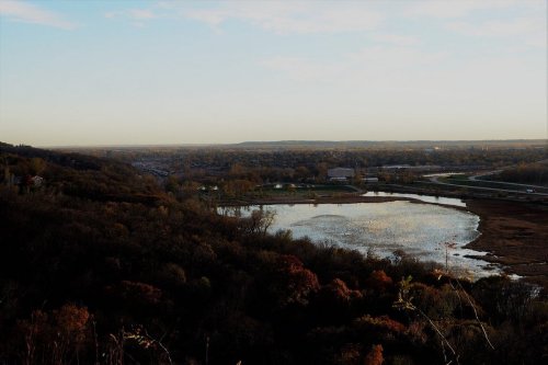 A scenic view of a calm lake surrounded by autumn foliage and distant hills under a clear sky.