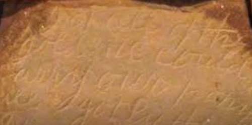 Close-up of an ancient stone tablet with faded, carved inscriptions in an unknown script.