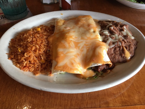 A plate of enchiladas topped with cheese, served with rice and refried beans on the side.