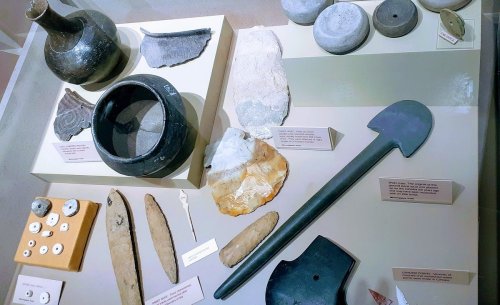 A display of ancient artifacts including pottery, tools, and stone items on a museum exhibit table.