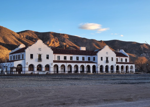 Historic white building with arched windows, set against mountains under a clear blue sky.