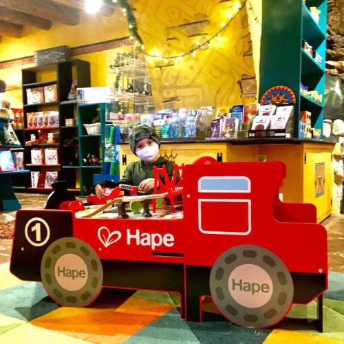 A child plays with a toy car in a colorful store filled with games and toys.