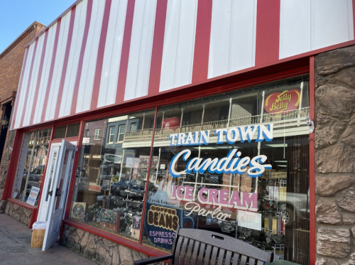 A storefront with red and white striped awning, featuring "Train Town Candies" and "Ice Cream Parlor" signs.