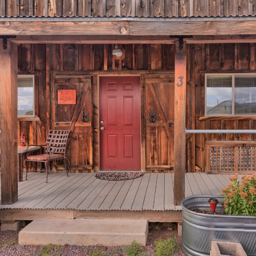 A rustic wooden cabin entrance with a red door, chairs, and a potted plant on the porch.