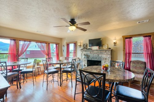 Cozy dining area with round tables, a stone fireplace, and large windows draped in red curtains, overlooking a scenic view.