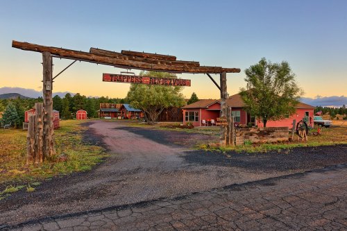 A rustic entrance sign for "Trapper's Haven" with a gravel road leading to a red building and surrounding trees.