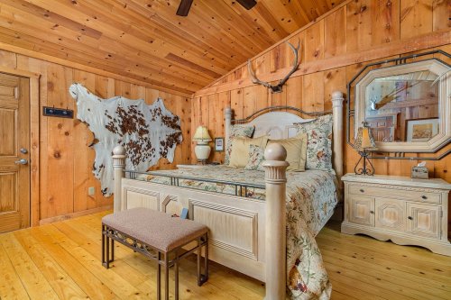 Cozy wooden bedroom with a bed, decorative antlers, and rustic decor, featuring a wooden floor and wall art.