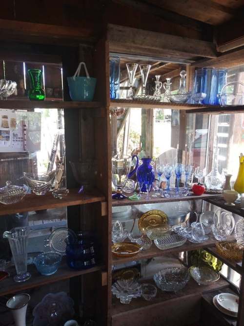 A wooden display shelf filled with various glassware, including vases, bowls, and decorative pieces in different colors.
