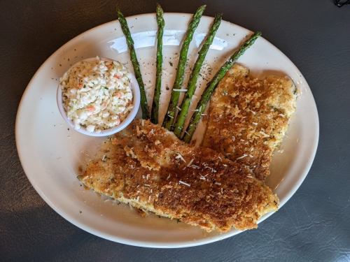 A plate featuring two breaded fish fillets, asparagus spears, and a side of coleslaw.