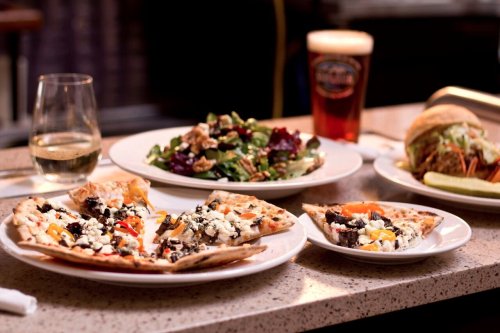 A table setting with three pizzas, a salad, and a glass of wine, alongside a pint of beer.
