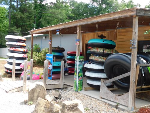 A shed displaying various colorful inner tubes for sale, surrounded by trees and gravel.