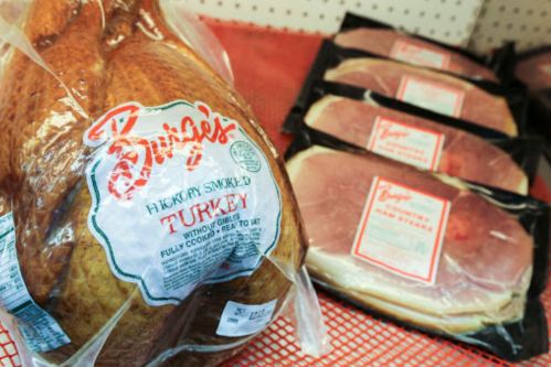 A package of hickory smoked turkey next to several packs of sliced ham on a red display.