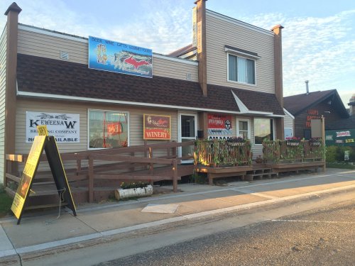 A storefront with signs for a brewery and winery, featuring a wooden deck and colorful banners, under a clear sky.