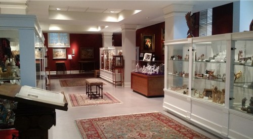 A spacious museum gallery featuring display cases of artifacts, a wooden table, and decorative rugs.