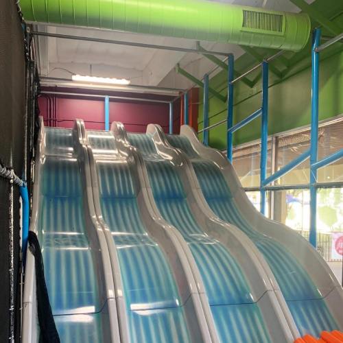 Indoor play area featuring three colorful, wavy slides with a bright green and purple backdrop.