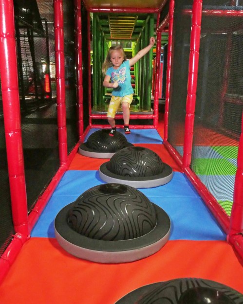 A child navigates a colorful indoor play structure, stepping on black, wavy platforms.
