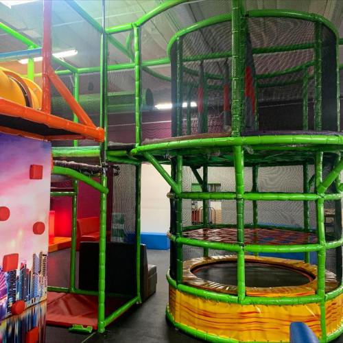 Colorful indoor play structure with climbing areas, nets, and a trampoline, designed for children's activities.