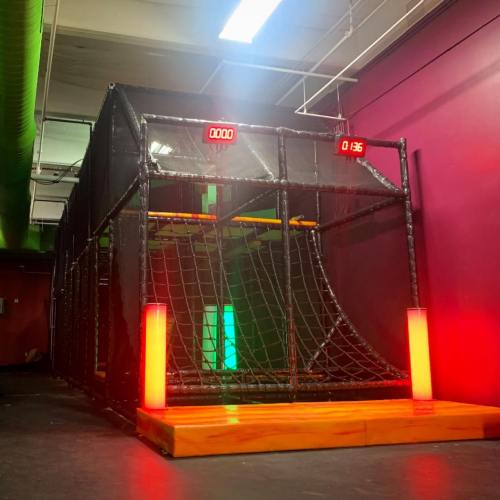 A sports arena with a netted enclosure, featuring a timer and illuminated columns, set against a colorful wall.