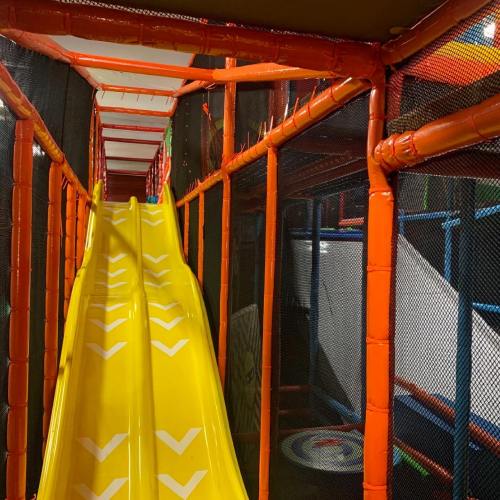 A bright yellow slide in a colorful indoor play structure with netting and various climbing areas.