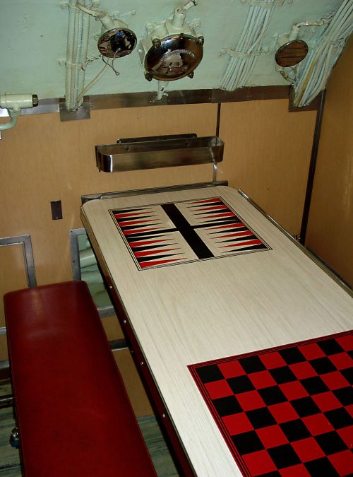 Interior of a submarine featuring a table with a black and red checkerboard design and a red bench seat.