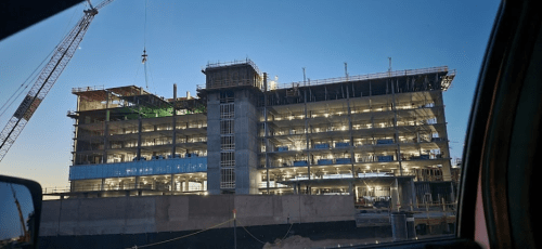 Construction site of a multi-story building at dusk, with cranes and scaffolding visible.