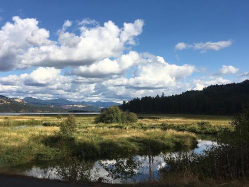 A serene landscape featuring a calm lake, lush greenery, and mountains under a partly cloudy sky.