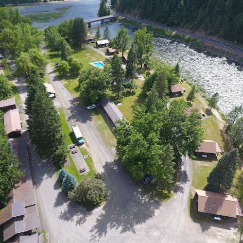 Aerial view of a riverside campground with cabins, trees, a pool, and a road along the water.