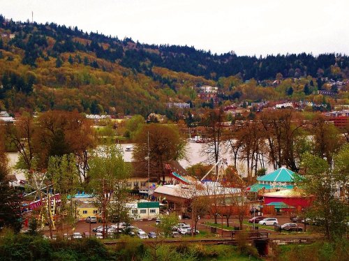 A scenic view of a park with rides, surrounded by trees and hills, under a cloudy sky.