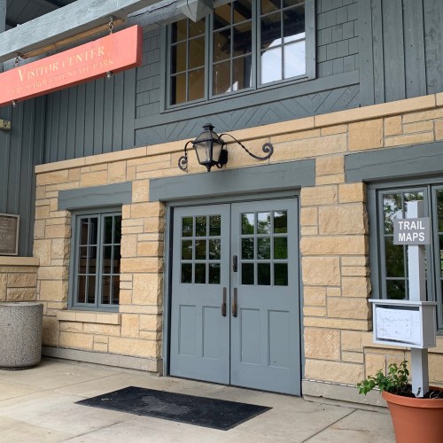 Exterior of a visitor center with a stone facade, large windows, and a sign above the entrance.