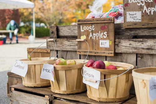 Baskets of loose apples labeled Cortland, Mac, and Empire at a farmers market stand.