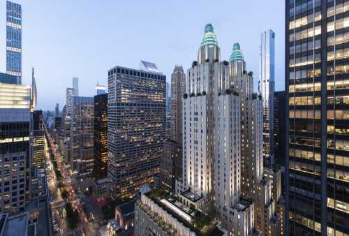 Aerial view of a city skyline at dusk, featuring tall buildings and a prominent art deco structure with green accents.