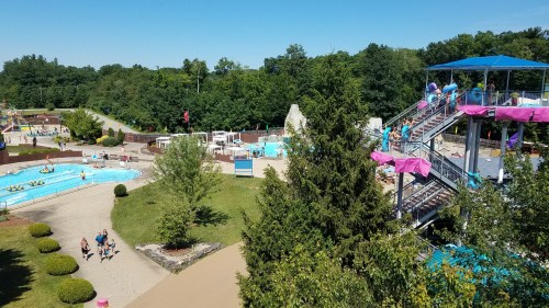 A sunny water park scene featuring slides, a lazy river, and visitors enjoying the attractions amidst greenery.