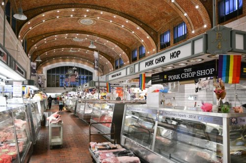 Interior of a bustling market featuring meat displays, with signs for "Pork Chop Shop" and colorful flags hanging.