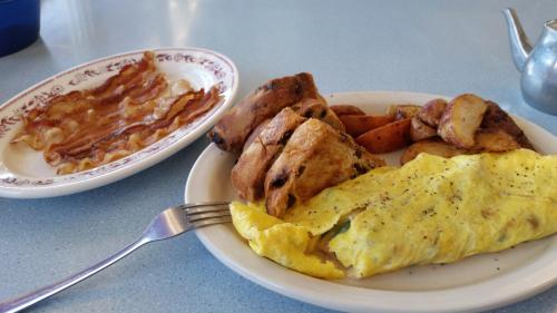 A plate with a fluffy omelet, roasted potatoes, and a side of crispy bacon and sweet rolls on a blue table.