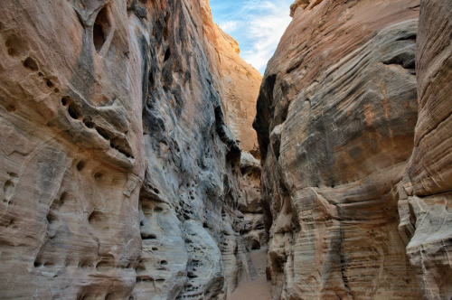 A narrow canyon with smooth, layered rock formations and a clear blue sky above.