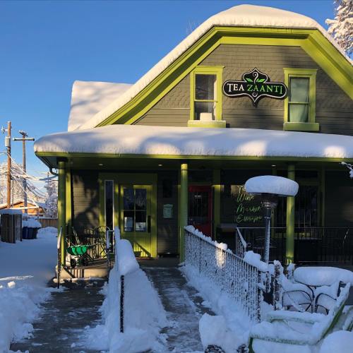 A cozy tea shop with a green and gray exterior, covered in snow, under a clear blue sky.