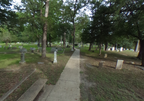 A peaceful cemetery path lined with gravestones, surrounded by trees and greenery.
