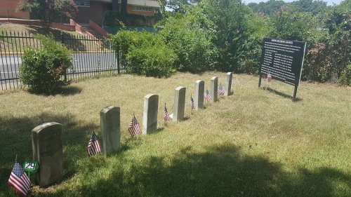 Grave markers with small American flags in a grassy area, alongside a sign listing names and information.