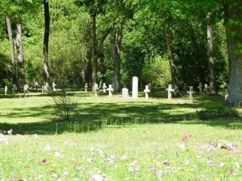 A serene cemetery with white crosses among trees, surrounded by green grass and colorful flowers in the foreground.