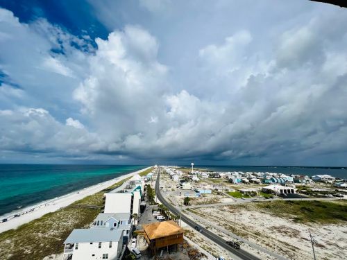 A coastal view featuring sandy beaches, a road, and a mix of homes under a cloudy sky.