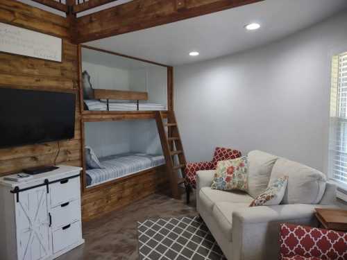 Cozy living space with a sofa, decorative pillows, a TV, and a bunk bed nook with blue-striped bedding.