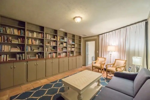 Cozy living room with bookshelves, a blue sofa, two armchairs, a coffee table, and soft lighting.