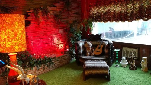 Cozy room with a vintage chair, guitar, plants, and decorative items, illuminated by warm red and yellow lighting.