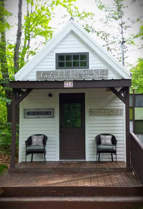 A small white gatehouse with a peaked roof, featuring two chairs on the porch and signs for "Chocorua" and "Wonalancet."